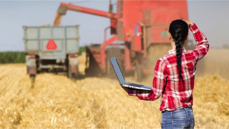 Farmer with laptop looks at farming equipment