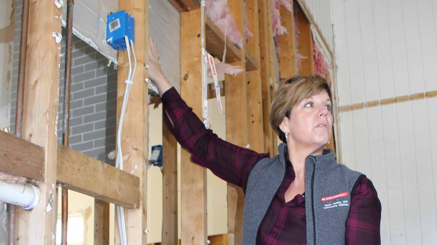 Sarah Kirby pointing to drywall behind exposed wooden studs in a flooded home.