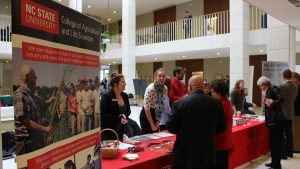 NC State poster and people gathered at exhibit table.