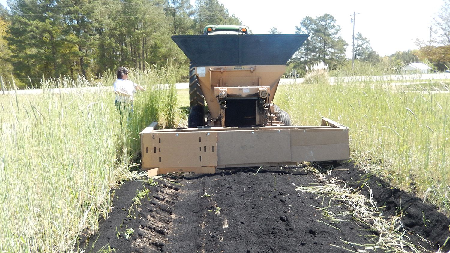 Tractor in a field, spreading black biochar in a 10-foot row.