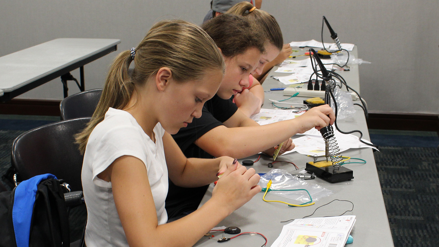 Several 4-H'ers at a table, practicing soldering.