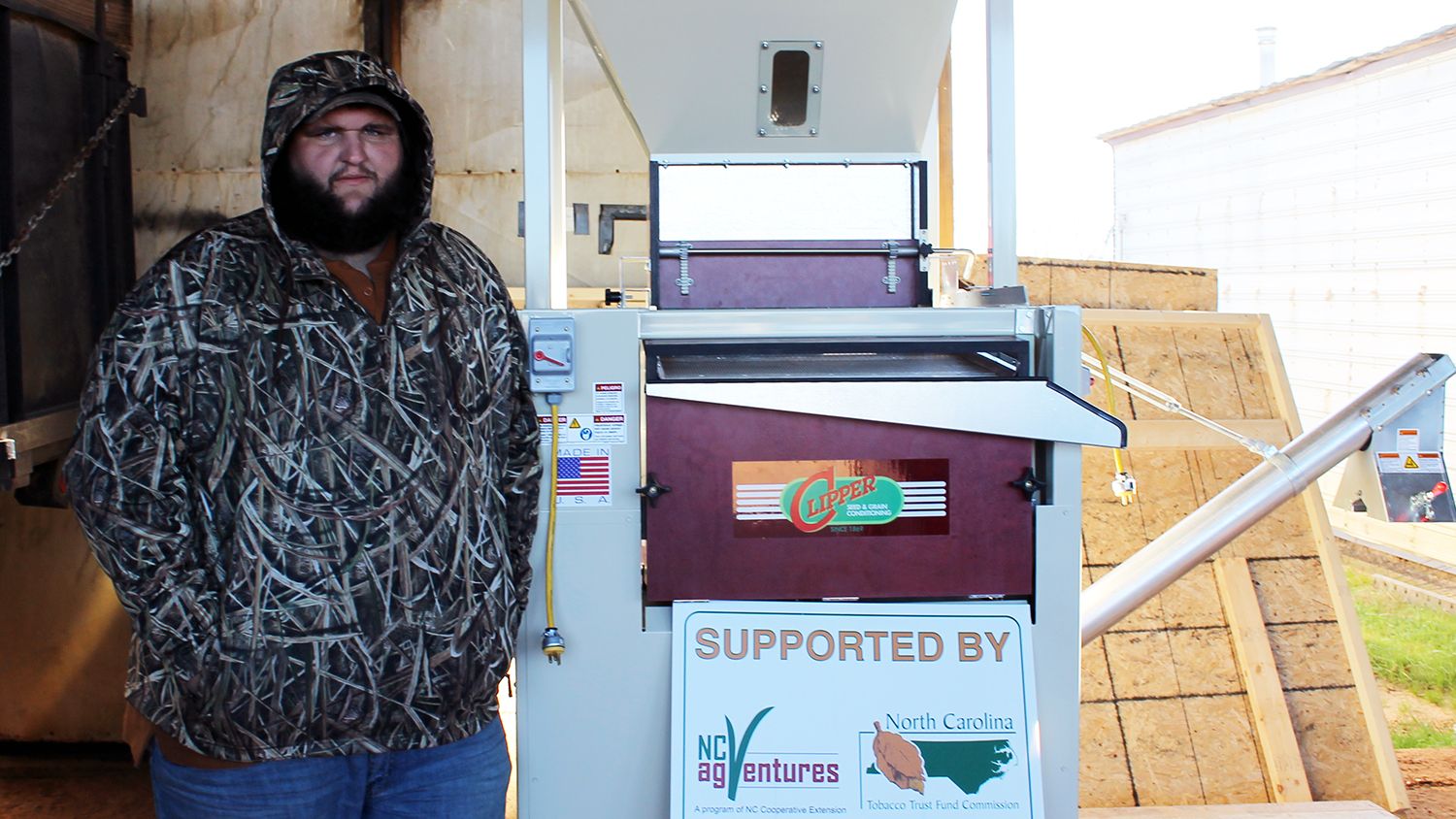 Farmer standing beside a popcorn cleaning machine.