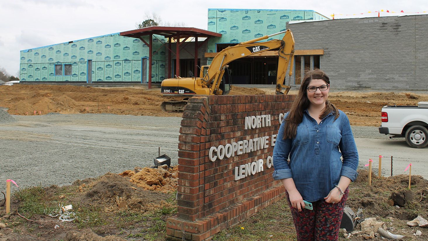 Woman behind North Carolina Cooperative Extension Lenoir County sign, at the construction site for the new county center.