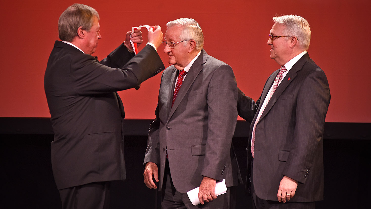 NC State Board of Trustees chair Jimmy Clark (left) places the Watauga Medal over the head of 2018 recipient Bill Collins as Chancellor Randy Woodson (right) looks on.