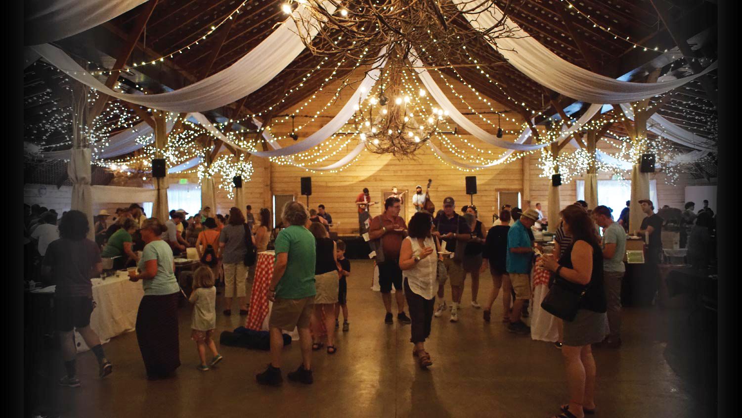 group of people enjoying a party in a barn with lights.