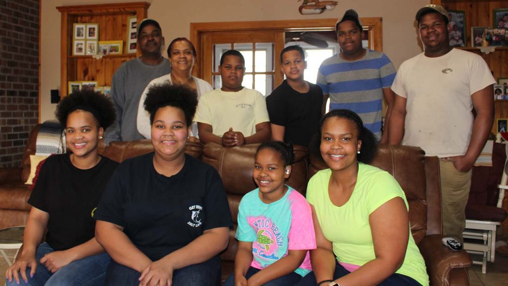 9 family members, four sitting on a couch in front, with six standing in the back row.