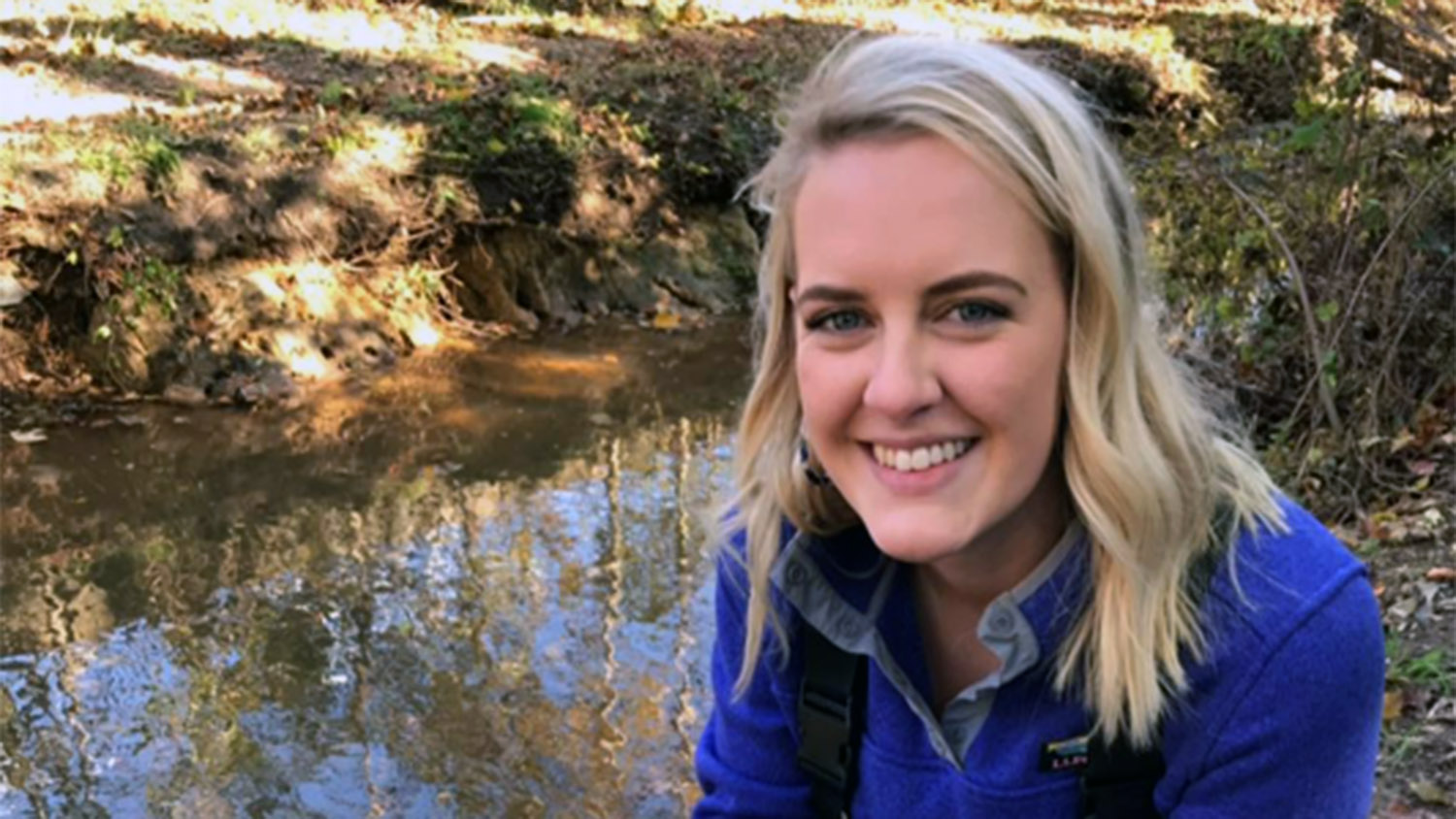 Applied Ecology's Emilee Briggs stands next to a stream in the forest