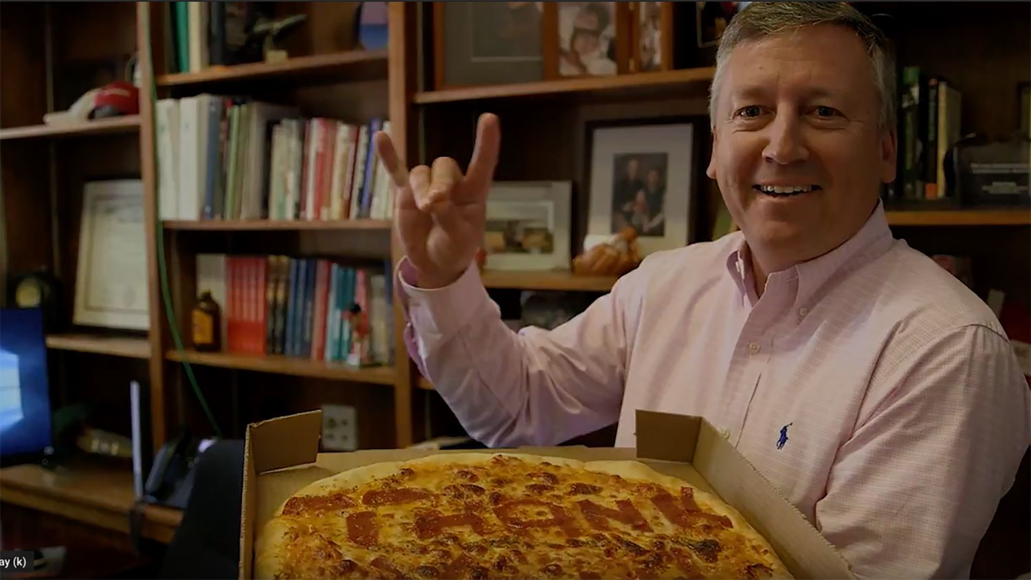 Dean Richard Linton holding a thank-you pizza and giving the Wolfpack sign.