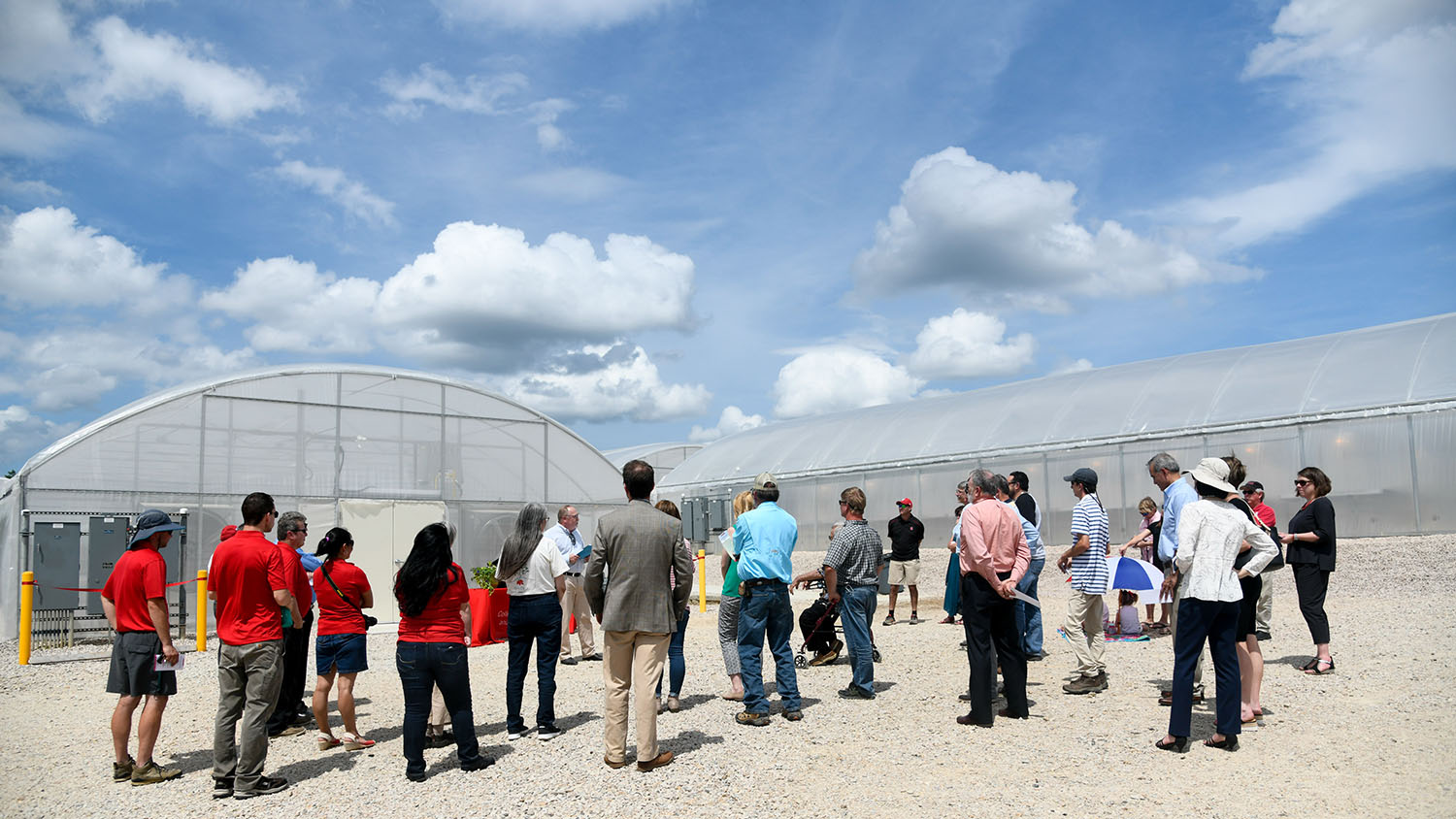 Group of adults gathered outside of greenhouses listening to a speaker