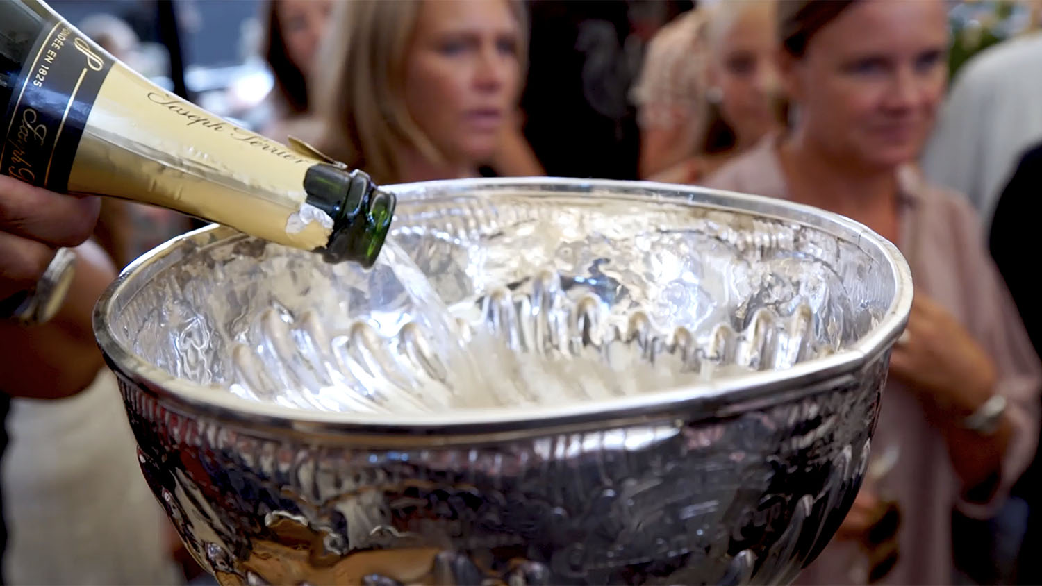 Someone pouring champagne into the Stanley Cup with two women in the background.