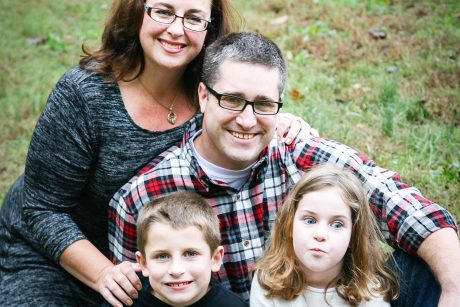U.S. Army Major Drew Reinbold-Wasson, his wife and their son and daughter in a family portrait in a field. Reinbold-Wasson is wearing a plaid shirt and glasses.