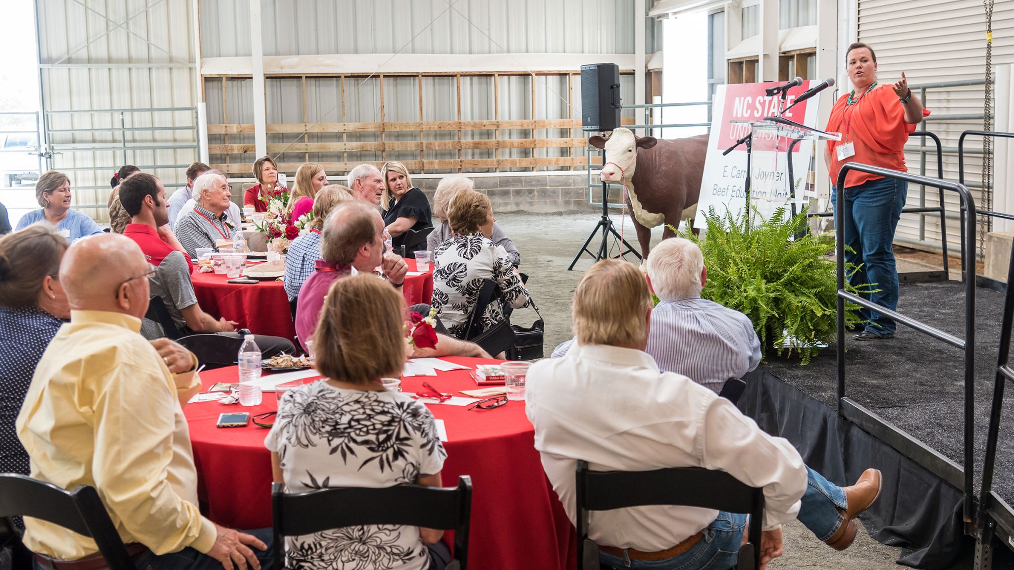 People sitting in a cattle show pen watching a presentation.