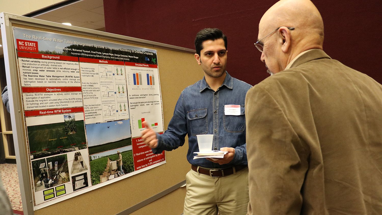 Two men talking in front of a poster