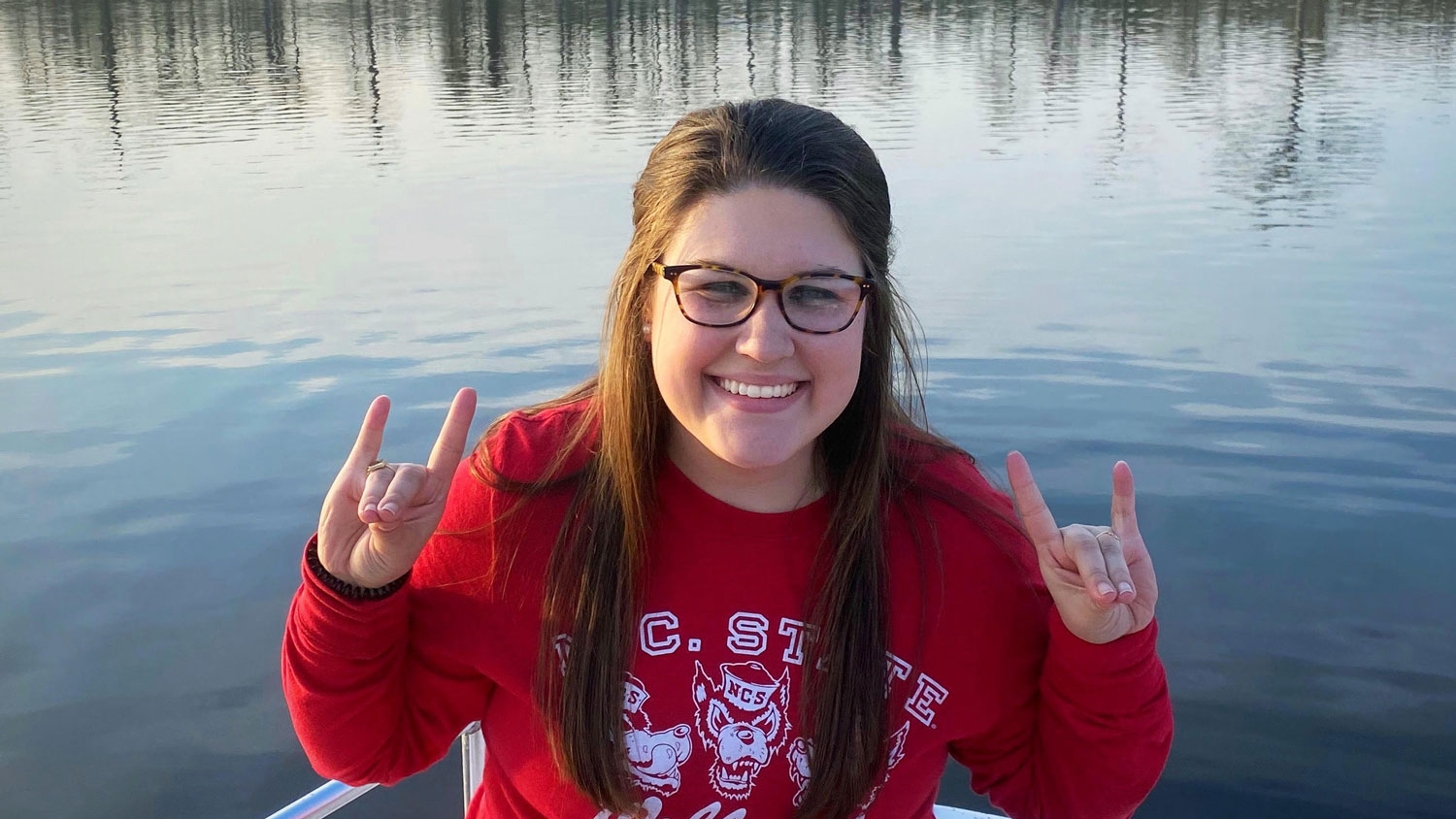 Young woman sitting on a small boat in the middle of water with two wolfpack hands