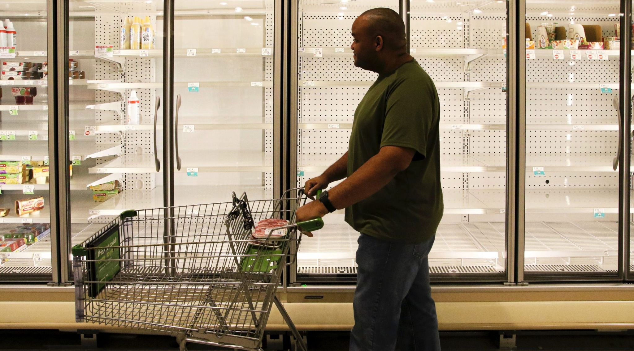 Supermarket shopper pushing cart past empty refrigerator cases