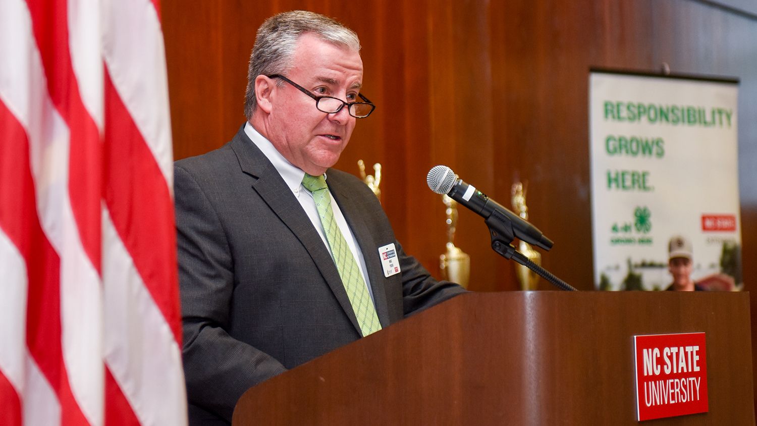 Flag, man at podium and 4-H banner