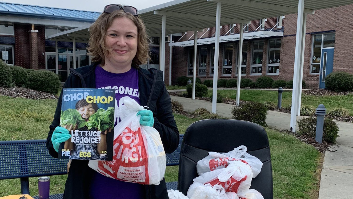 White female outside a school holding a magazine and grocery bags