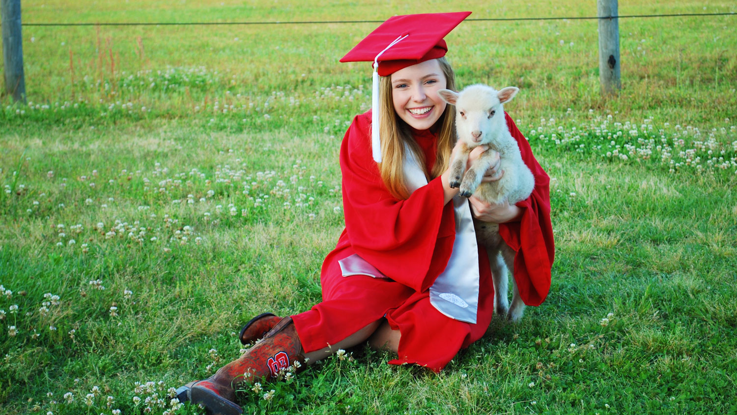 Young woman in a red cap and gown holding a goat