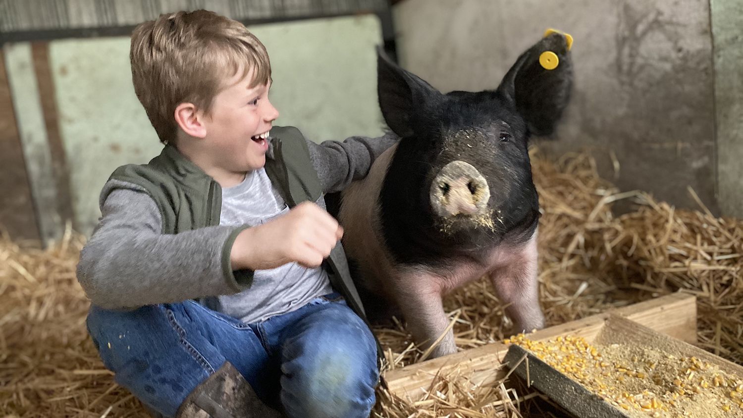 Smiling child with his arm around a pig