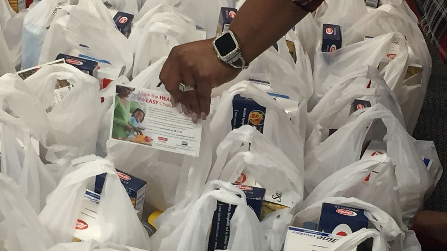 A person's hand puts an information card into a bag of food.