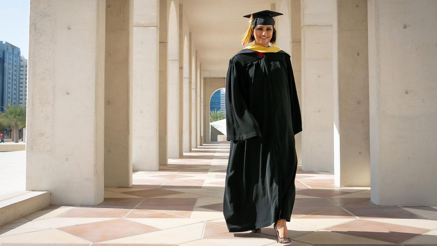 A woman walking, wearing a black cap and gown