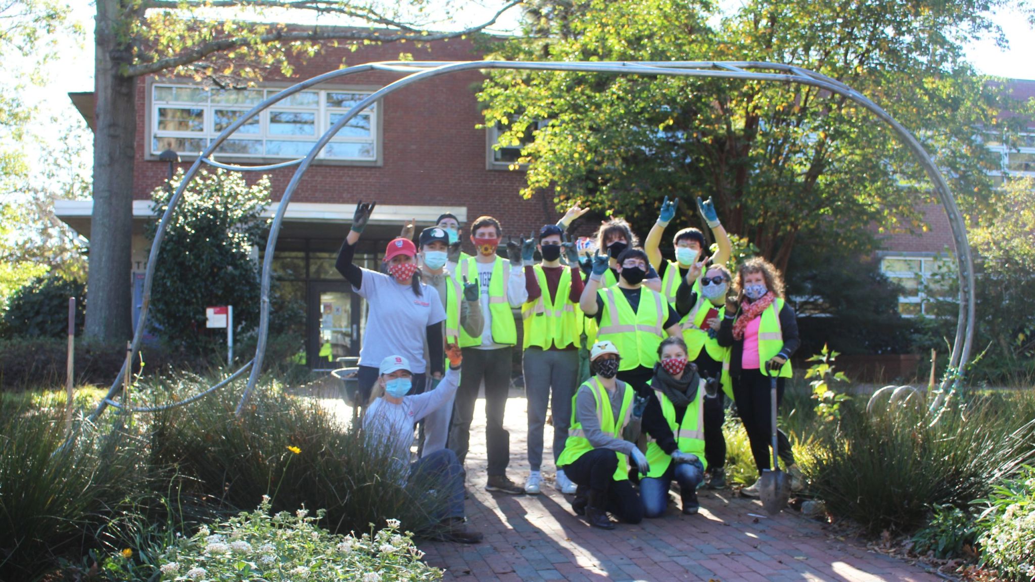 The class shows their wolf hands under the Kilgore Hall arbor