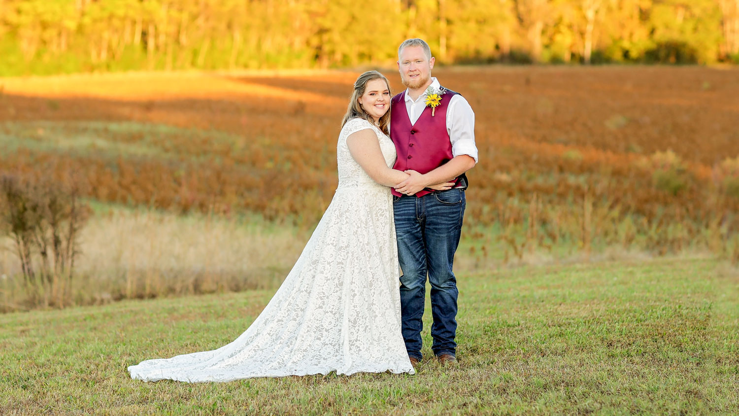 A young married couple standing in a field.