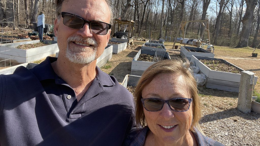 Man and woman in front of several raised beds for growing vegetables and fruit.