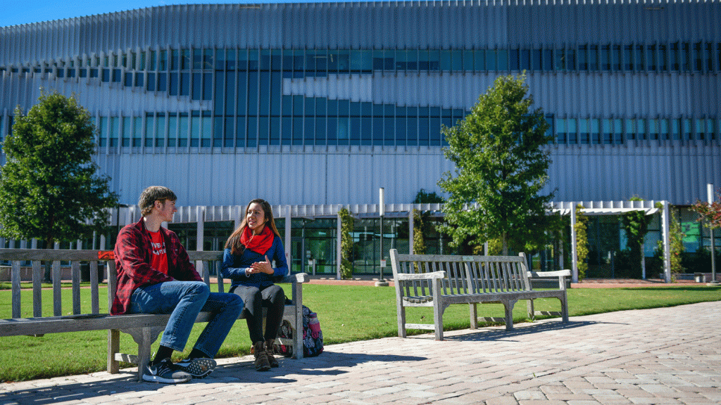 Two students sitting on a bench in front of a glass building