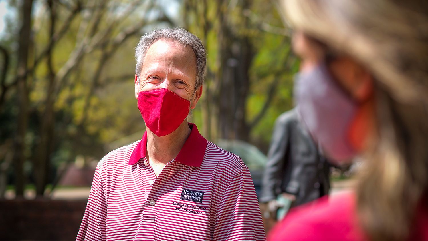 Man with mask talks to student outdoors