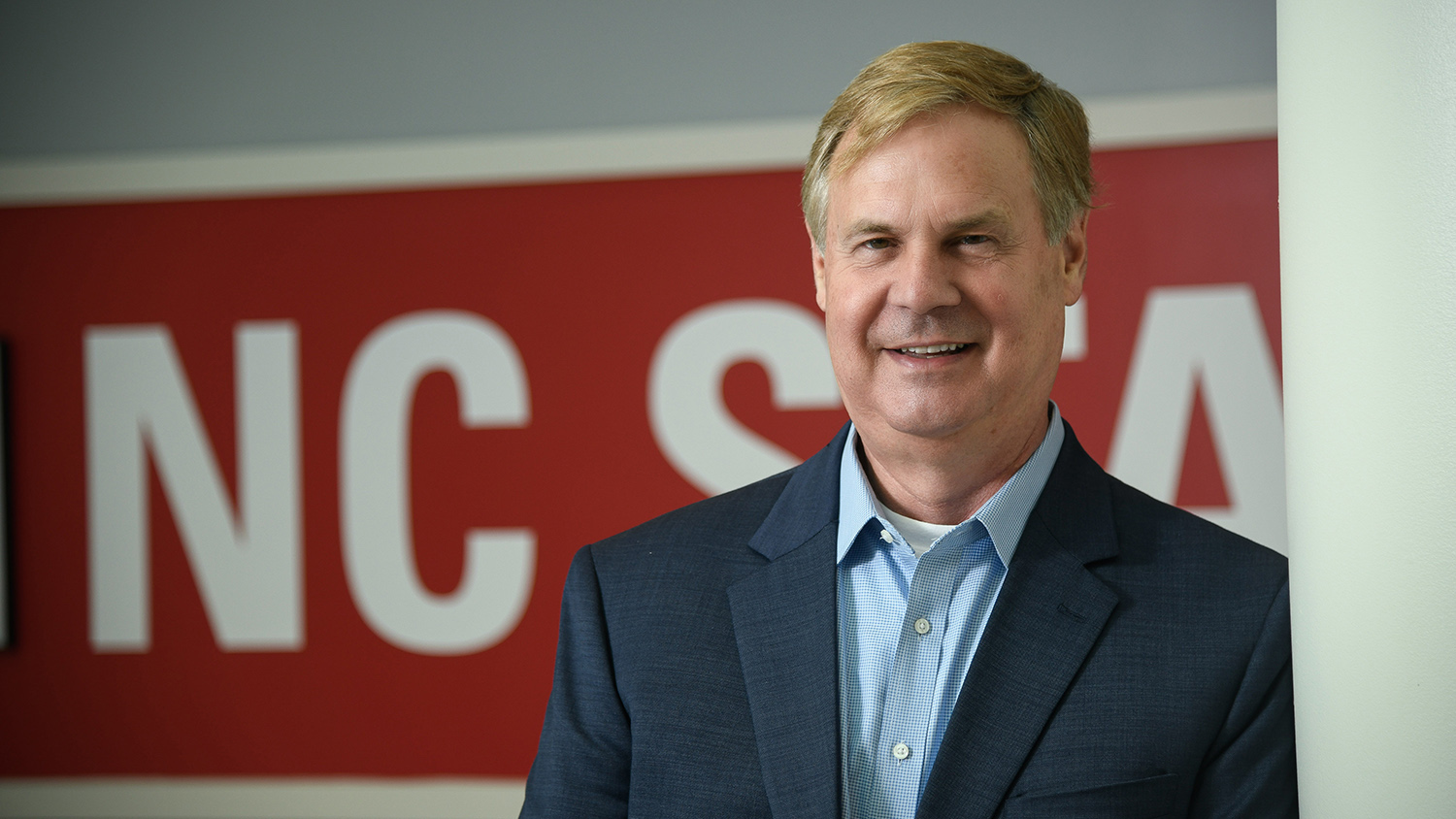 Man leaning against pillar, with the NC State logo on a wall behind him