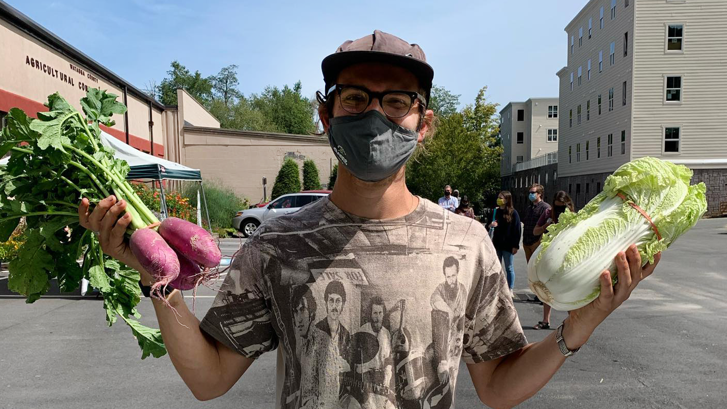 A man wearing a mask and holding up fresh produce