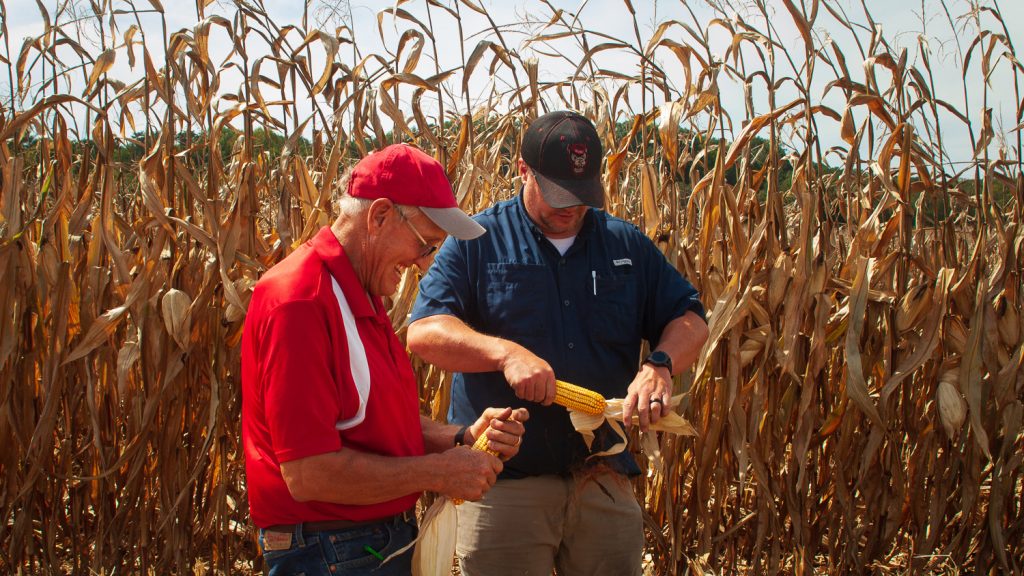 A father and son hold corn in a field