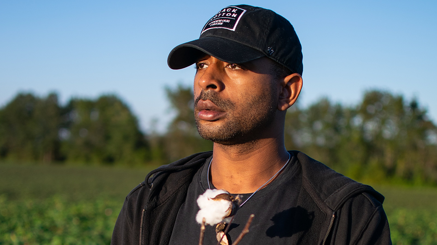 A Balck man standing in a field holding cotton