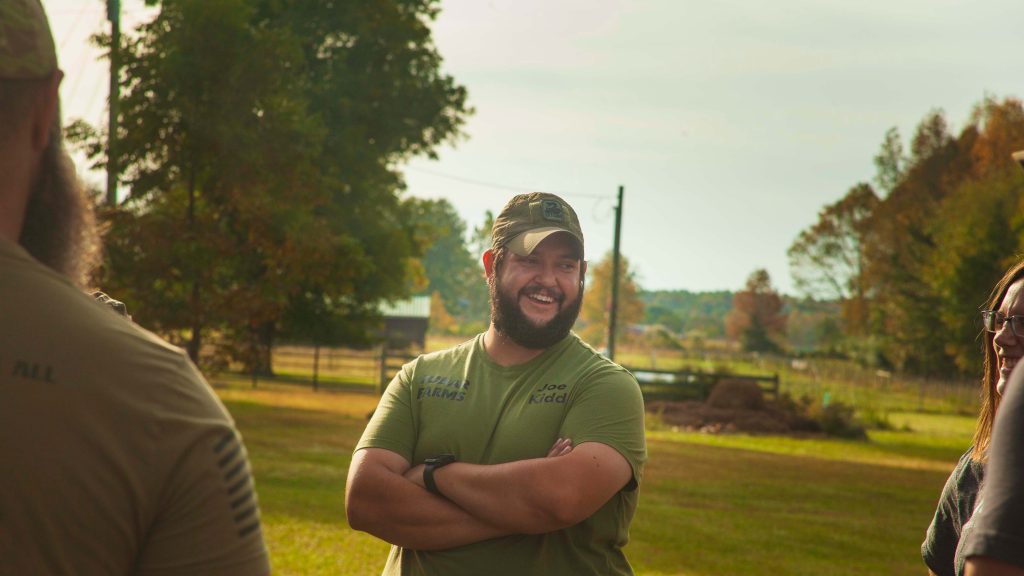 Joe Kidd smiles on his farm with his arms crossed.