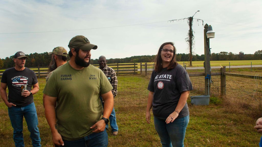 Sara and Joe Kidd talk on their farm with friends in the background.