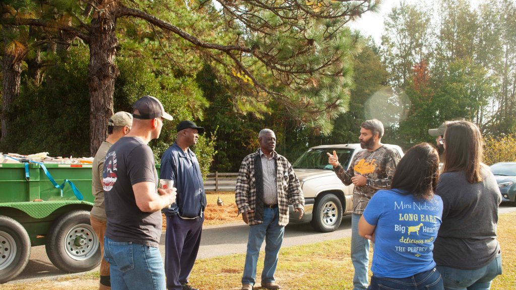 A group of veteran farmers stand in a circle and talk with one another.