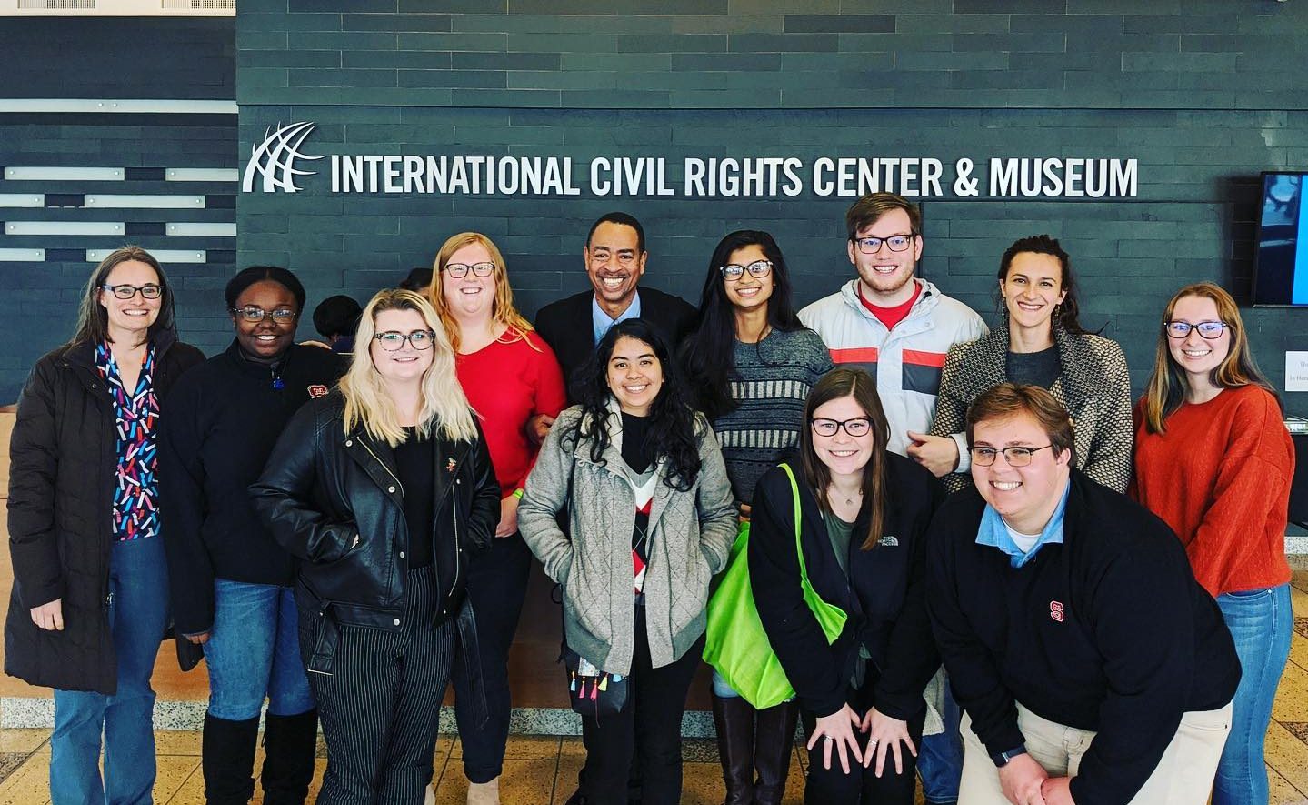 group of people posing in front of the International Civil Rights Center and Museum