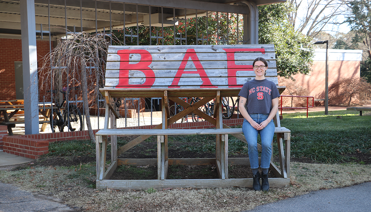 a young woman standing in front of a sign that says BAE