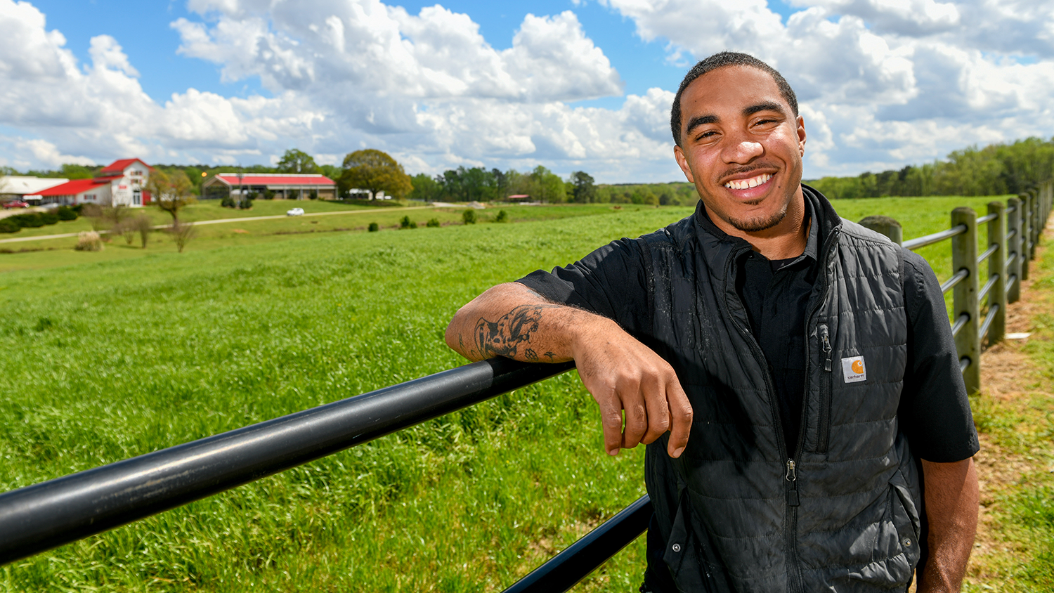 Male student leaning on fence in field