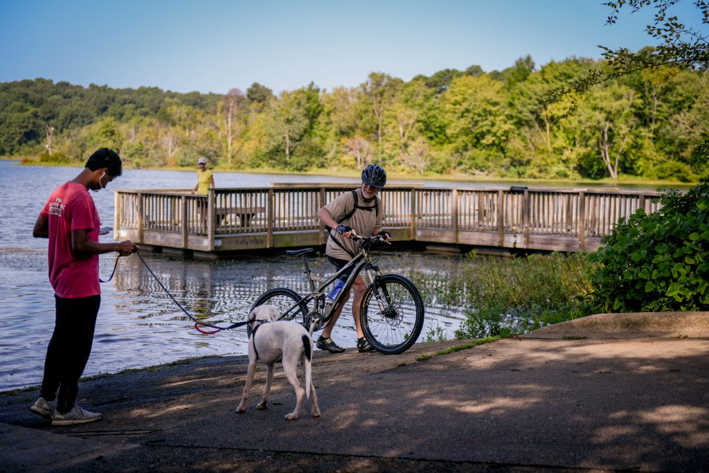 A biker, dog, and man by Lake Raleigh Woods.