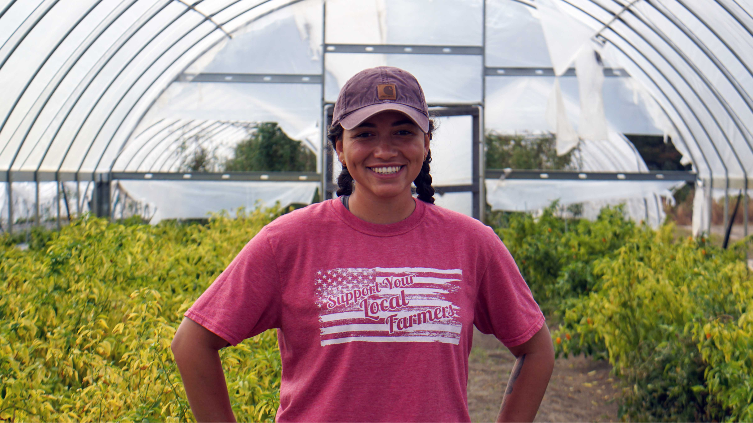 Marlena Chieffo standing in a greenhouse wearing a shirt that says "Support your local farmers"