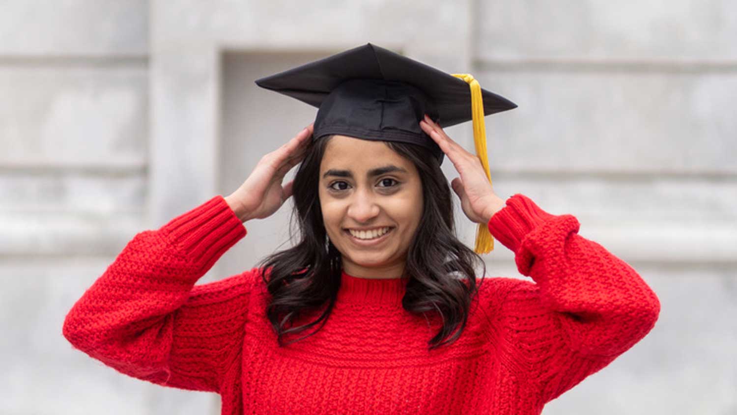 Young female student wearing a red sweater and graduation cap