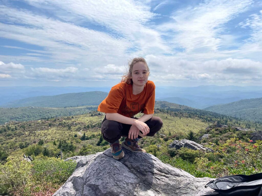 a young woman squatting on top of a mountain peak.