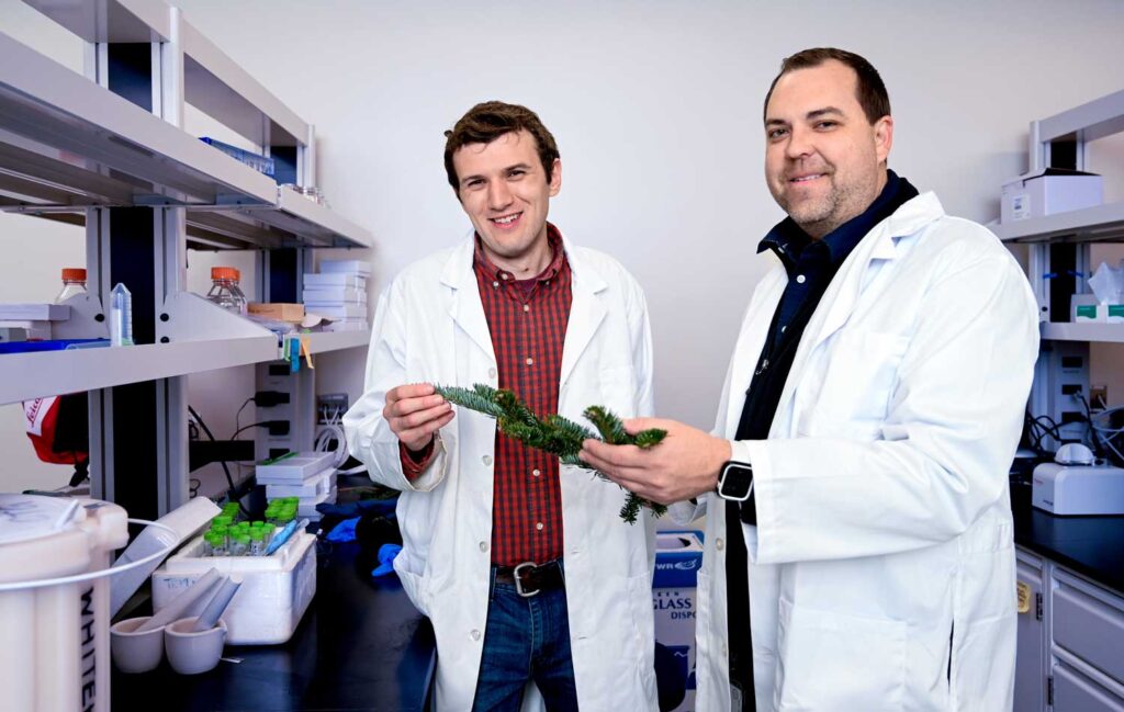 Two men in white lab coats holding a small Fraser fir branch.