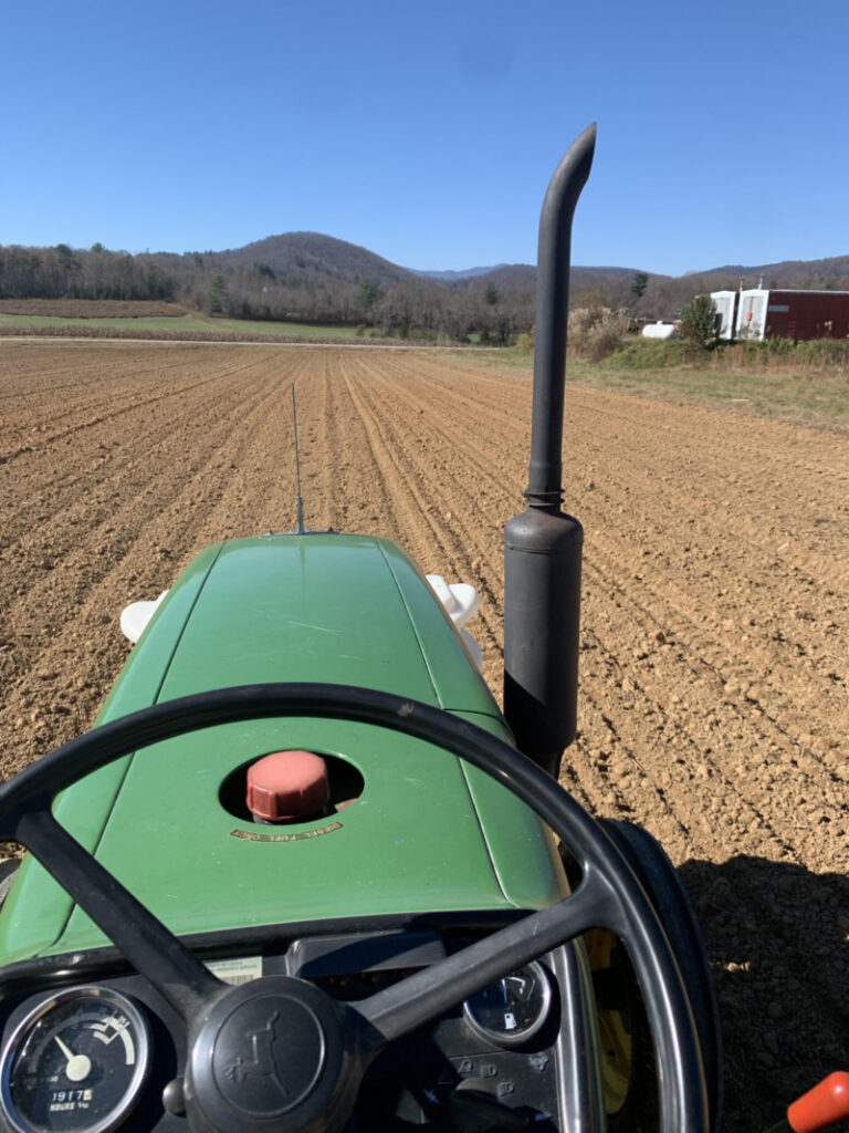 A view of someone riding a tractor in a field with mountains on the horizon