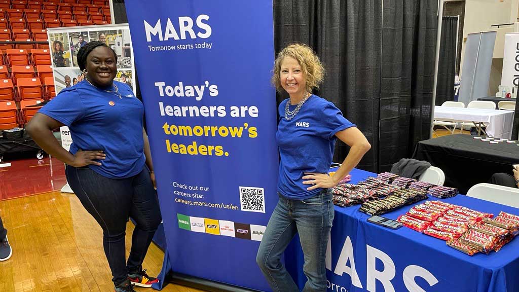 Two women standing next to a banner at a career fair