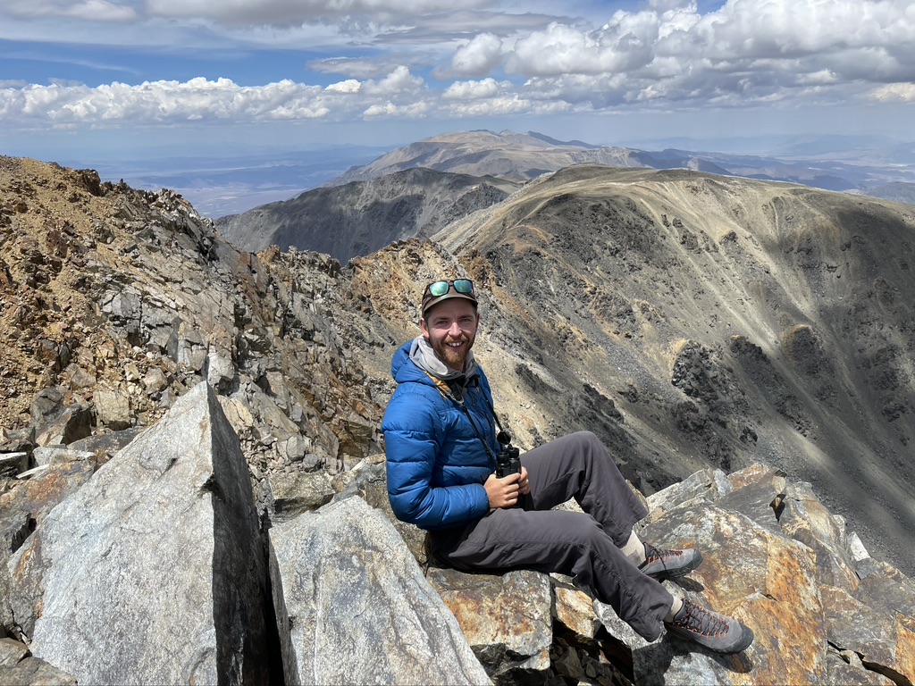 Kaleb Goff holding binoculars on a mountain