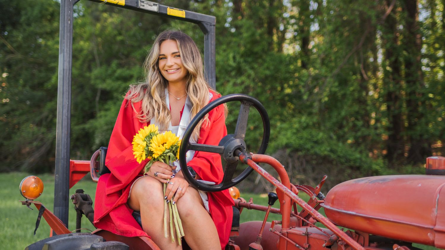 Abby Pleasant holding sunflowers in her graduation gown on a tractor