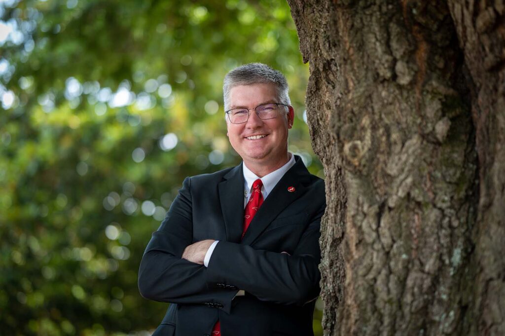 Man in a suit leaning against a tree and smiling